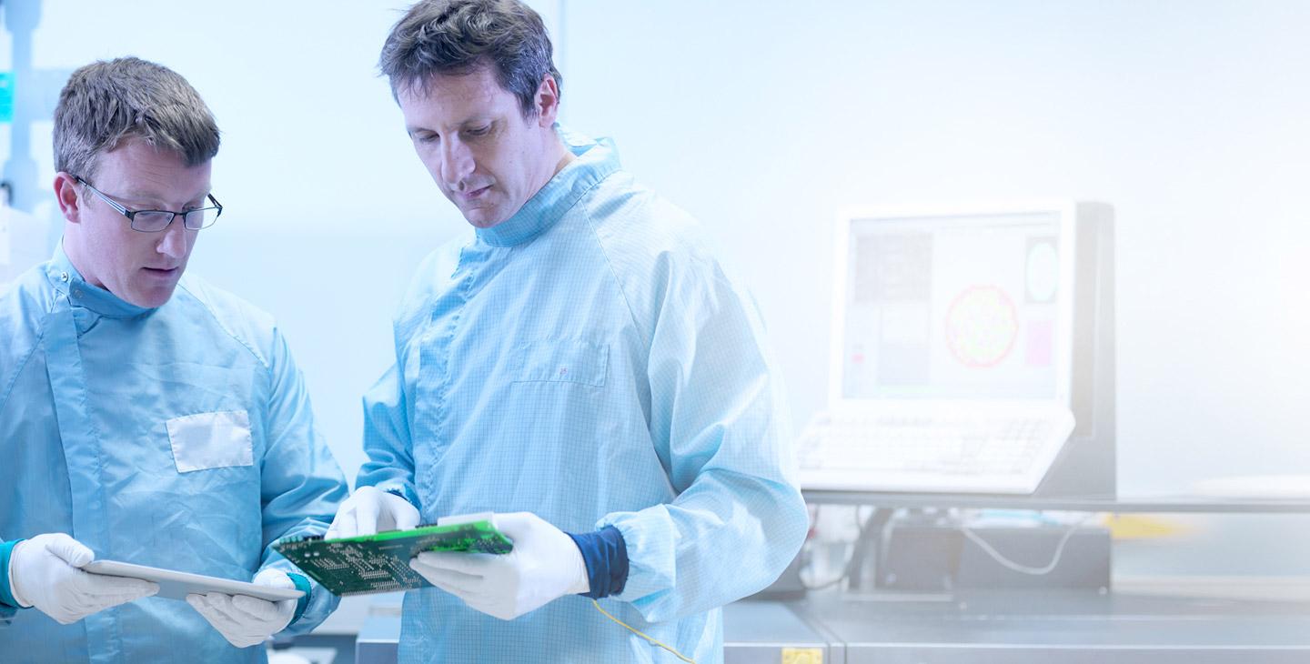 两个穿着实验室制服的人戴着乳胶手套看着半导体，一个拿着平板电脑